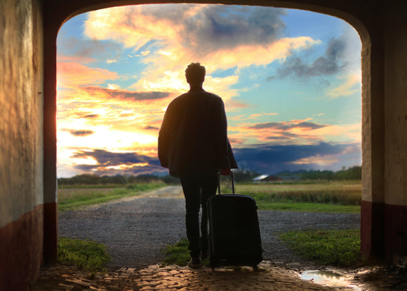 Person walking out into the sunrise with suitcase beginning their journey