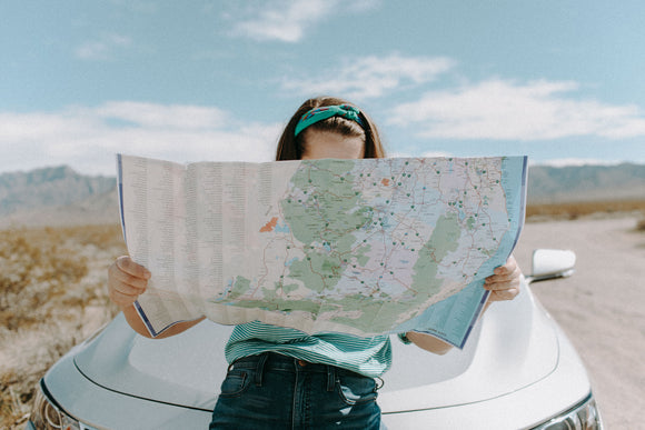 Person lost on a road in the desert looking at a map while leaning on the front of their car. 